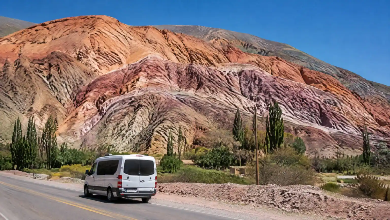 Private transfer car driving through the colorful Quebrada de Humahuaca landscape in Jujuy, Argentina